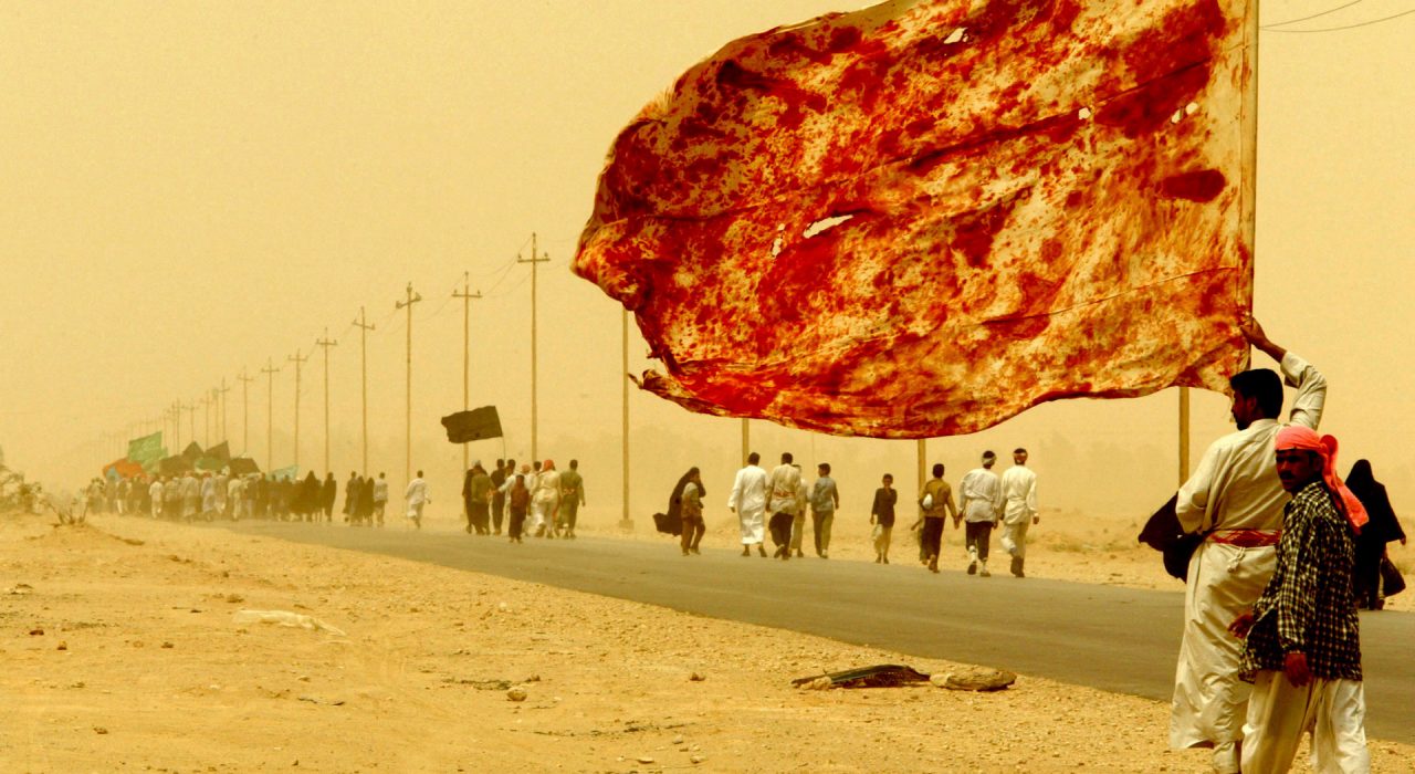 An Iraqi Shiite man carries a flag stained with the blood of men who wounded themselves to demonstrate their love to the Imam, as he walks along with tens of thousands of religious Iraqi's on their way to the central city of Kerbala through a sand storm April 19, 2003. Thousands of Iraqi Shi'ite Muslims beat their chests with their hands and waved black and green flags in a passionate celebration of a religious pilgrimage banned for a quarter century under Saddam Hussein. Men in robes and women draped in flowing black chadors streamed along narrow lanes and through palm tree orchards from towns and villages in southern Iraq to Najaf, from where they will go on to the city of Kerbala to mark one of the holiest events in the Shi'ite calendar, on April 23. REUTERS/Yannis Behrakis/File photo
